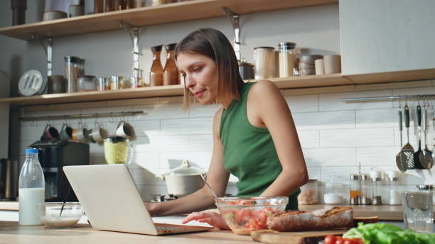 istock Chewing woman working computer in home kitchen at morning. Lady drinking coffee 2177326735