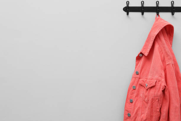 Coral jacket hanging on coat rack on light grey wall, space for text