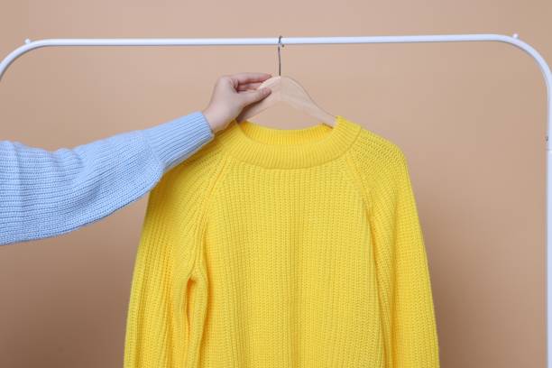 istock Woman taking yellow sweater from rack on beige background, closeup 2177329078