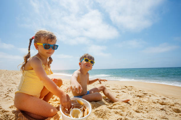 Kids happily playing with seashells on beach under the sunny sky