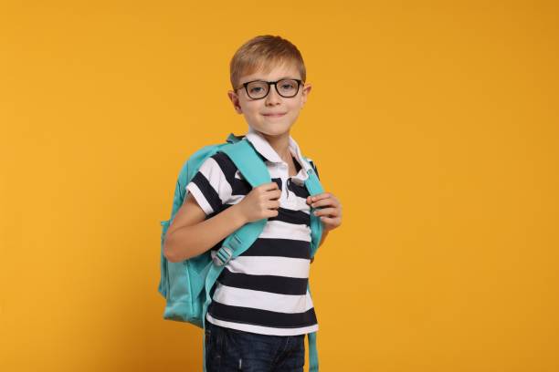 istock Happy schoolboy in glasses with backpack on orange background 2177334478