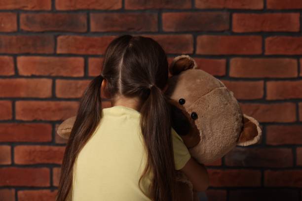 istock Upset little girl with teddy bear near brick wall, back view 2177334595