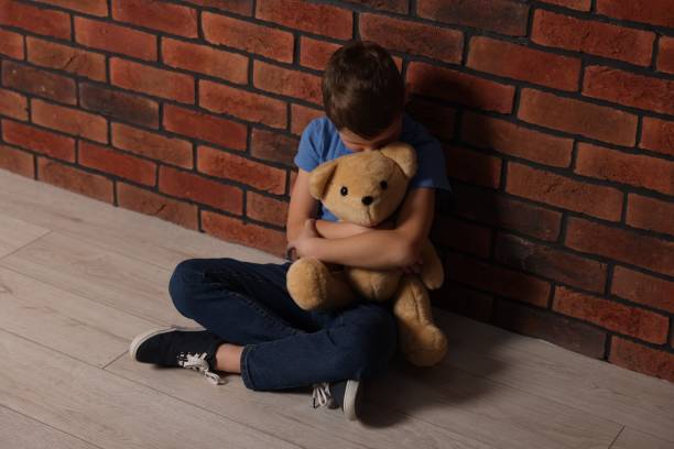 istock Upset boy with teddy bear sitting on floor near brick wall indoors 2177334614