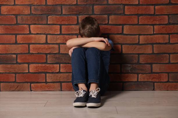 istock Upset boy sitting on floor near brick wall indoors 2177334689