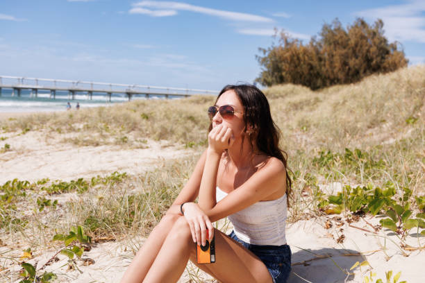 istock Young woman sitting on the beach holding a disposable camera 2177339320