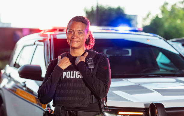 Multiracial policewoman standing with patrol car Portrait of a mature, multiracial policewoman standing outdoors in front of her police car, smiling at the camera. She is mixed race African-American, Asian and Hispanic, in her 40s. female police officer stock pictures, royalty-free photos & images