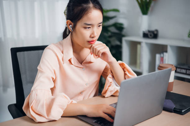 istock Young asian woman sitting at desk thinking idea while working on laptop in modern office. 2177344402