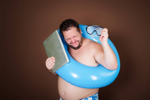 Side view of a young man relaxing by the pool on a summer day and reading a book on an e-reader.