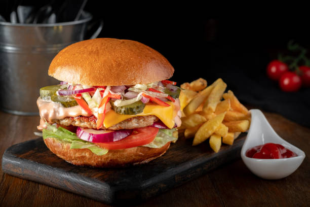 istock Large hamburger with bbq cutlet, Cheddar cheese, cabbage, pepper, tomatoes and onions. French fries and ketchup on a wooden table 2177354149