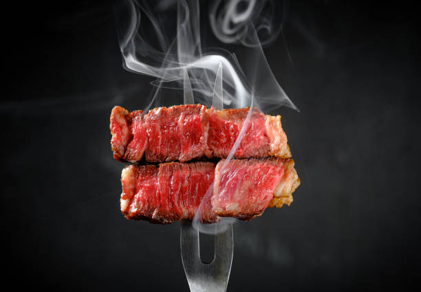 istock Grilled beef steak striploin on fork with smoke on dark background, close up 2177359011