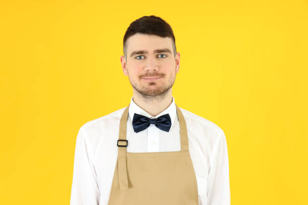 Concept of occupation, young waiter on yellow background