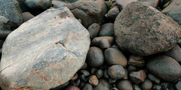 A close-up view of various smooth and textured rocks arranged naturally. The photo captures both large and small rocks with differing shades of gray and brown, highlighting their rough surfaces.