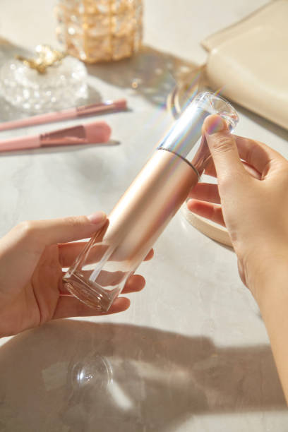 istock The minimalist chic space showcases a model hand holding a clear, white, copper gradient mockup of lotion bottle for viewing. Pink brushes rest beneath the table, behind a glass box and a white purse. 2177369740