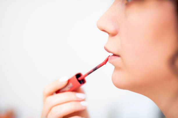 Copy space shot of smiling mid adult businesswoman sitting at the office and looking at the hand mirror while applying lipstick.