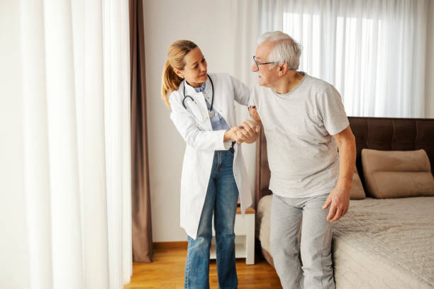 istock Caring doctor is helping sick old man to get up from a bed during her visit. 2177381693