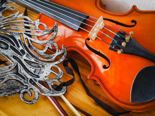 Violin put beside fancy mask on wooden board,show detail of acoustic instrument.
