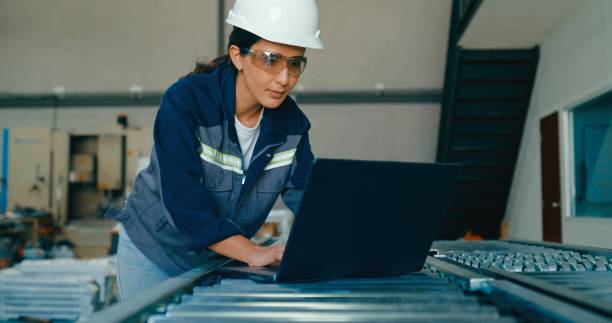 istock Young female engineer wearing hardhat uses laptop to analyze data and manage operations in factory. Robotic Industrial Factory. 2177383969