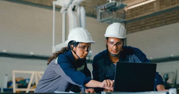 istock Two young engineers wearing safety gear analyze data on laptop and documents in robotics factory, focusing on precision and innovation. Robotic Industrial Factory. 2177384012