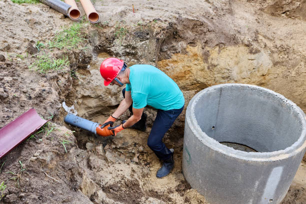 istock Plumber inserts bent fitting into socket of an underground sewer inlet pipe when installing septic tank made of concrete rings. 2177384724