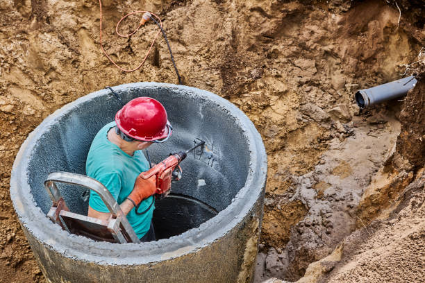 Worker uses corded rotary hammer drill with chisel for punching in concrete ring of septic tank.