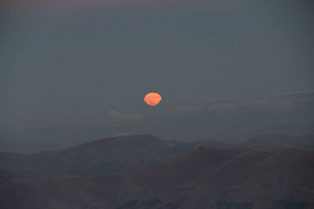 Rising orange moon over distant mountain ranges at twilight. Astronomy and nature concept.