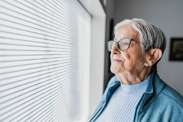 istock Senior woman looking through the window at home 2177388024
