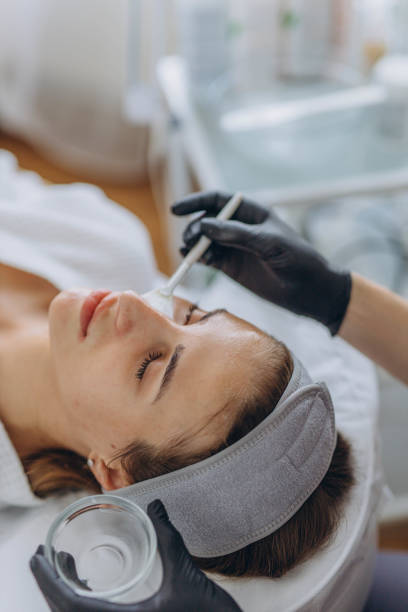 Cosmetologist performs a facial peeling procedure on a young woman.