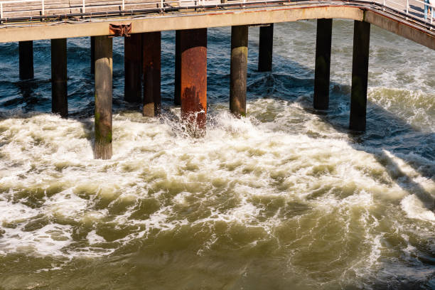 Rusty and weathered pillars of a pier. Waves break between the pillars. Rough North Sea, crashing waves, churning sea. Sunny day, beach at The Hague, Netherlands.