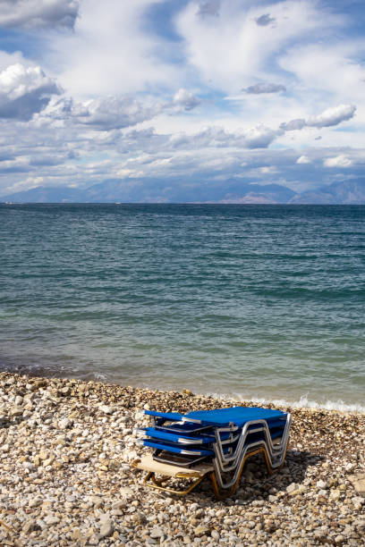 Coast of Ionian sea and a pebble beach. Pile of deck chairs. Blue sky with intense white clouds. North-East part of the island Corfu, Greece.