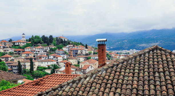 In Ohrid Macedonia charming rooftops of traditional houses create a picturesque skyline framed by mountains and an overcast sky showcasing the city's rich history.