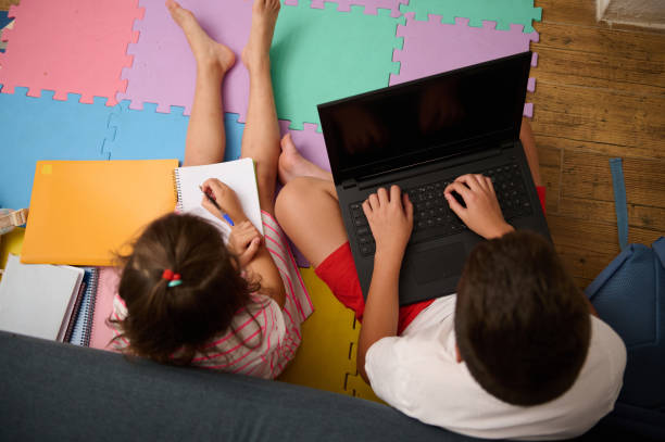 istock Children engaged in homework with laptop and notebooks on floor 2177397878