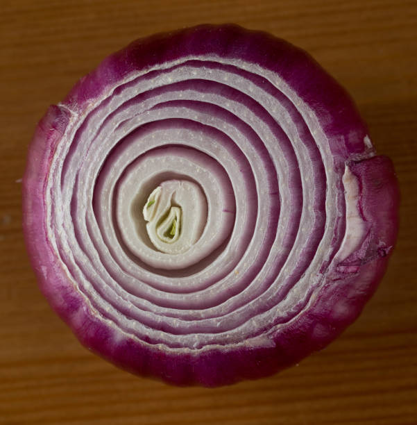 Stock photo showing a close-up view of healthy eating image of a wooden chopping board covered in red onion in various states of being cut up. Rings and sliced pieces of vegetables displaying purple skin and white flesh.