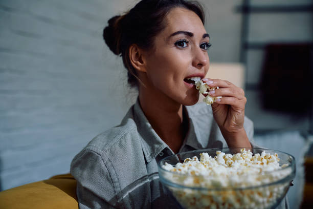 istock Young woman eating popcorn while watching TV at home. 2177400700