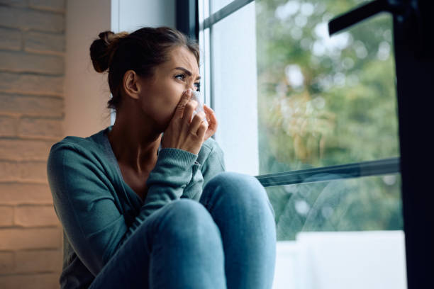 istock Ill woman blowing nose by the window. 2177401184