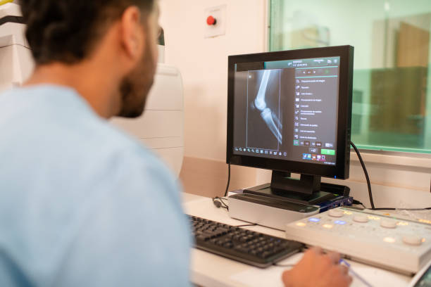 Rear view of doctor examining X-ray image on computer monitor.  Radiologist looking at knee x-ray image on computer screen in hospital.