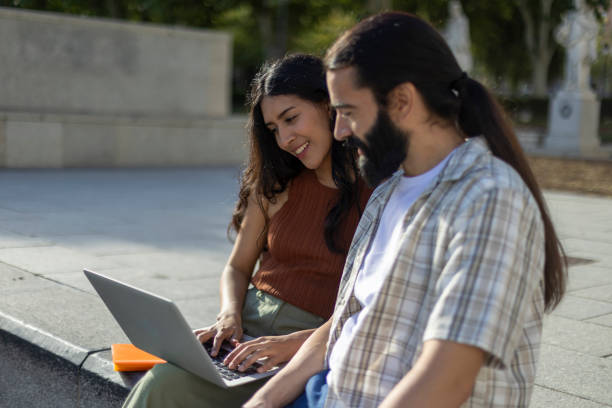 istock Young couple using laptop while sitting on bench in the city 2177426388