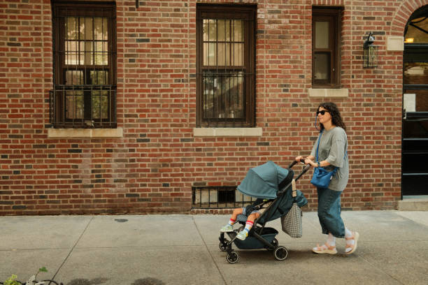 istock Mother pushing baby stroller walking on sidewalk in front of building 2177429331
