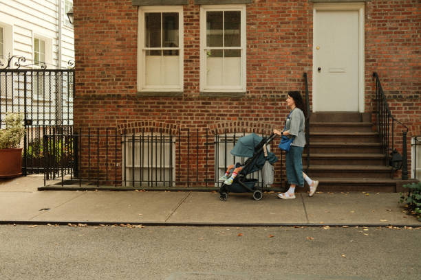 istock Young mother pushing stroller on sidewalk in front of brownstone building 2177429337