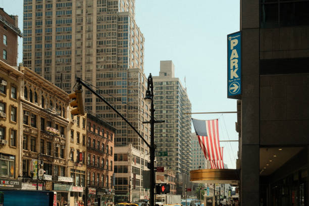 Yellow traffic light is changing as a taxi drives by in a busy downtown street of new york city with an american flag waving in the wind