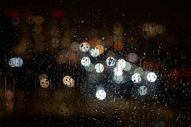 Raindrops on a window at night. Rain drops on glass window with night city lights on background, close-up
