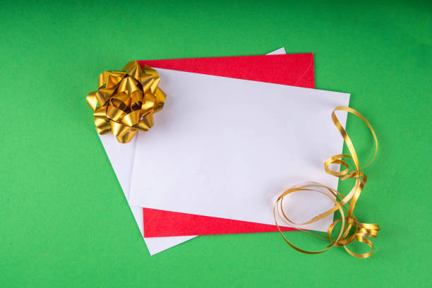 Santa's hand holding blank letter sheet of paper and envelopes on bright red green background. To-do list, wishlist, wishes, greeting card Christmas background top view copy space