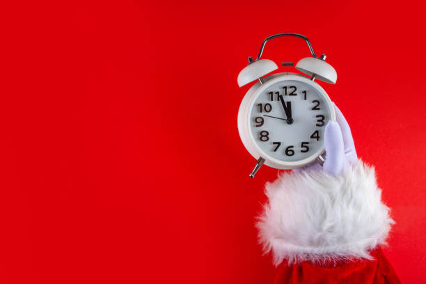 istock Santa Claus hand holding white alarm clock on red background 2177436382