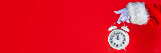 istock Santa Claus hand holding white alarm clock on red background 2177436392