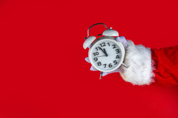 istock Santa Claus hand holding white alarm clock on red background 2177436398