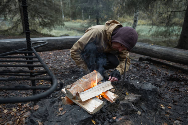 man starting a bonfire at picnic campfire in the forest