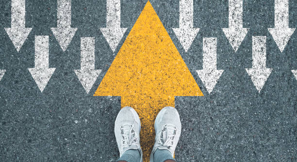 Man standing on yellow big arrow opposite  direction with white arrow on road asphalt for different thinking and Business and technology disruption concept.