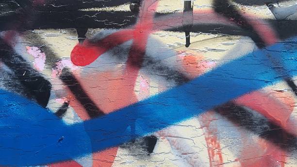 Blue, black and red spray painted graffiti close up on white wall, paint peeling, distressed and old.