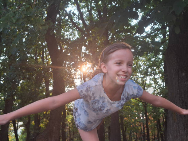 A girl balances while standing with arms outstretched on a wall in the park during summer day
