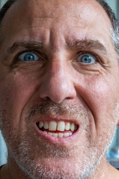 Close up of funny and weird, mimic and face expression of a man with blue eyes and stubble.