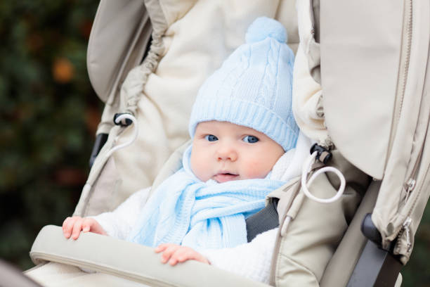 Baby boy in stroller. Child in pram in winter. Warm clothing for active walks with baby during cold season. Cute little kid in knitted hat and jacket sitting in pushchair. Infant in buggy.